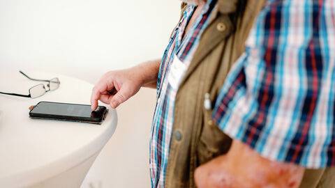 Älterer Mann beschäftigt sich mit Smartphone. Auf dem Tisch befindet sich eine Brille.