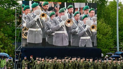 Eine Gruppe Soldaten steht vor einem Bildschirm, auf dem das Bundeswehrorchester zu sehen ist.