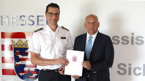 Innenminister Roman Poseck steht Felix Paschek und überreicht ihm eine Urkunde